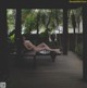 A naked woman laying on a wooden bench on a deck.