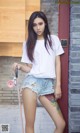 A woman in a white shirt and denim shorts holding a skateboard.