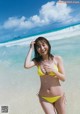 A woman in a yellow bikini standing on a beach.