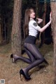 A woman in black tights and high heels leaning against a tree.