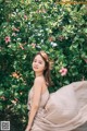 A woman in a long dress standing in front of a bush.