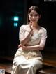 A woman in a white dress sitting on a wooden bench.