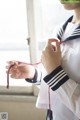 A woman in a sailor outfit tying a red ribbon.